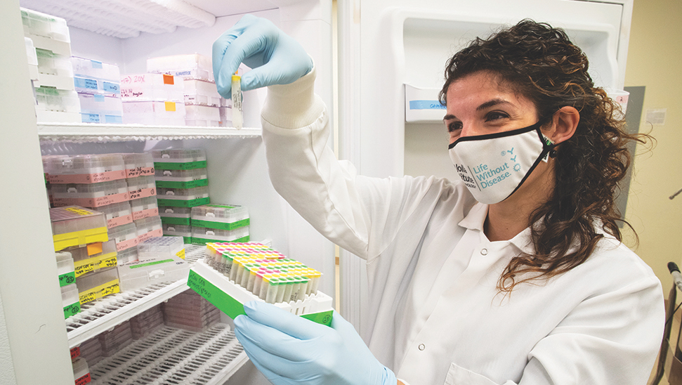 Photo of LJI Research Assistant Professor Alba Grifoni, Ph.D., holding up small vials in front of the freezer in a lab