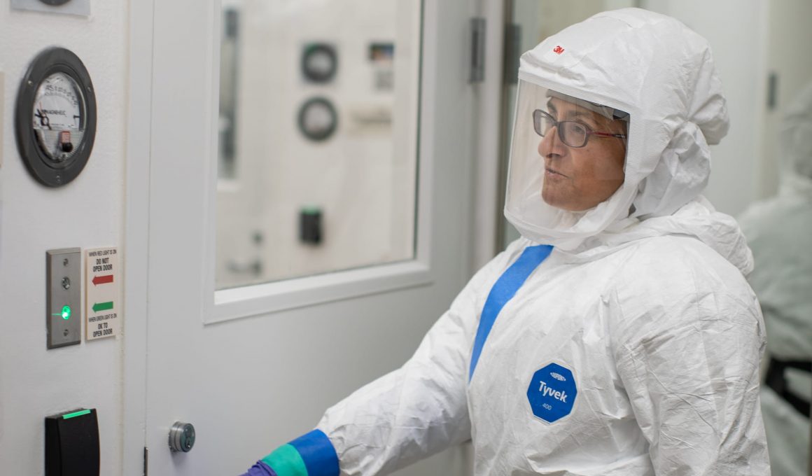 A scientist in a white high containment suit with a respiratory reaches to open a door at the LJI BSL-3 facility