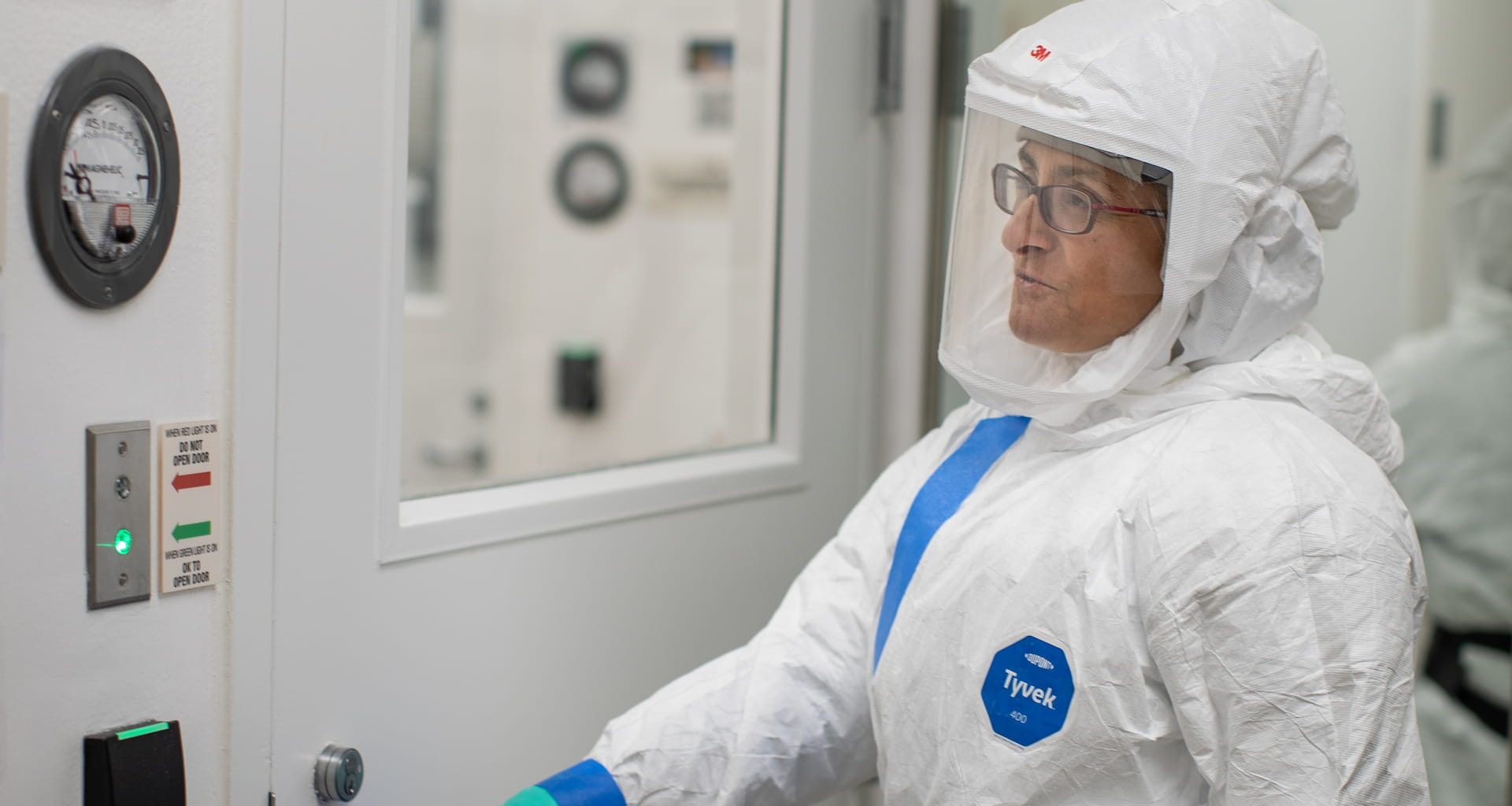 A scientist in a white high containment suit with a respiratory reaches to open a door at the LJI BSL-3 facility