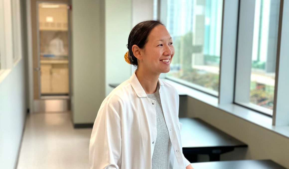 A woman in a white medical coat looks out a window