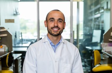 Dr. Reina sits in his laboratory. He is wearing a white lab coat and looking at the camera