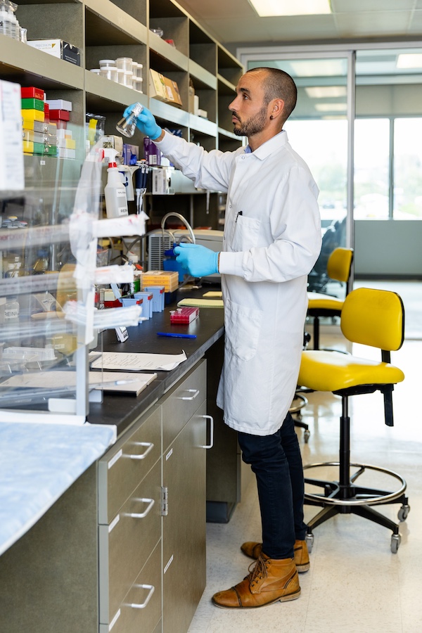 Dr. Reina working in the lab. He is wearing a white lab coat and blue gloves