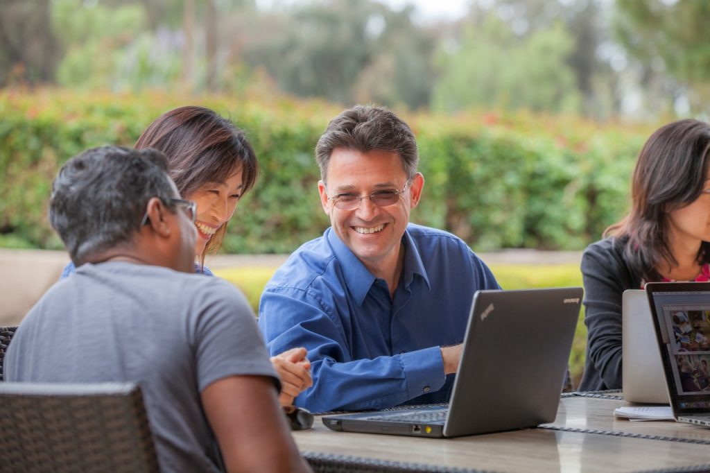 Dr. Croft sits at a table outside the Institute. He is smiling and interacting with other scientists.