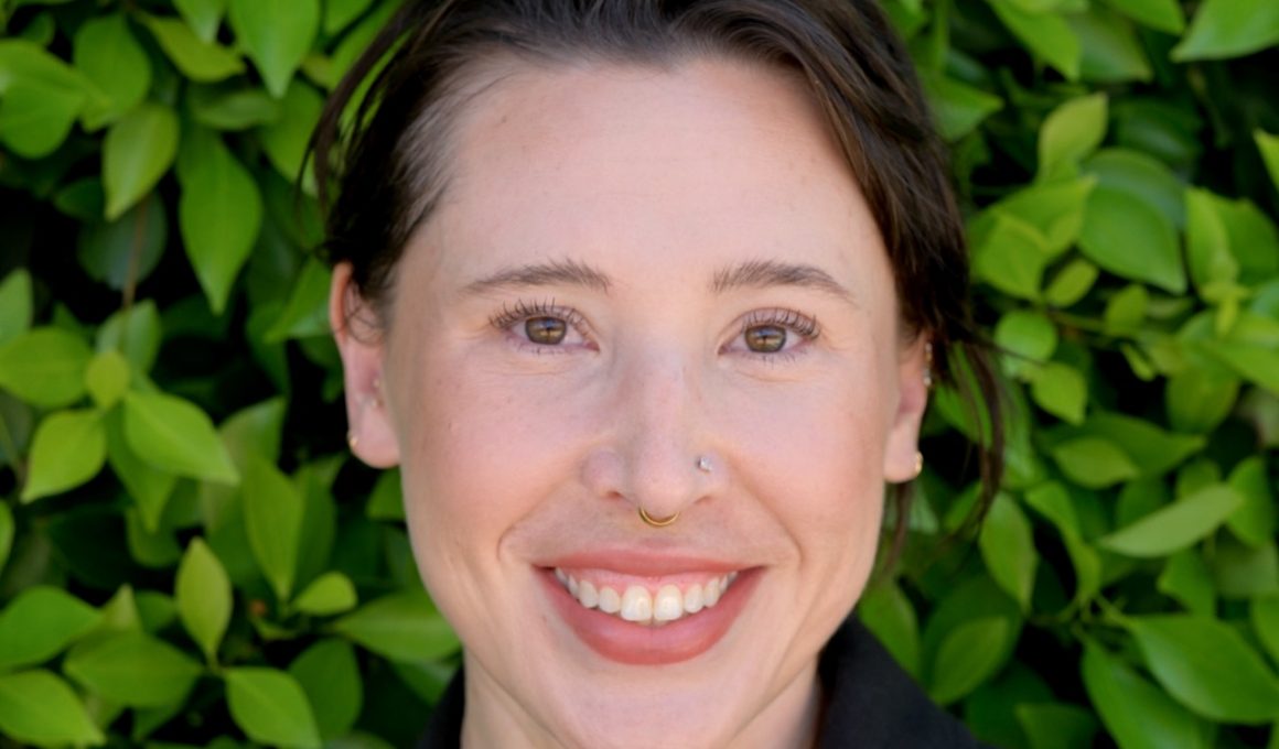 Portrait photo of Dr. Moderbacher. She is standing in front of green plants and smiling.