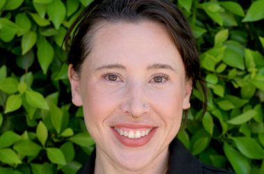 Portrait photo of Dr. Moderbacher. She is standing in front of green plants and smiling.