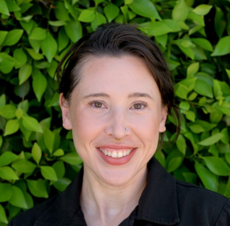Portrait photo of Dr. Moderbacher. She is standing in front of green plants and smiling.